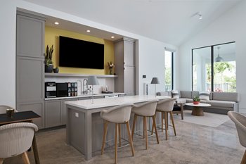 A kitchen and living room with a large white island with stools and a yellow accent wall